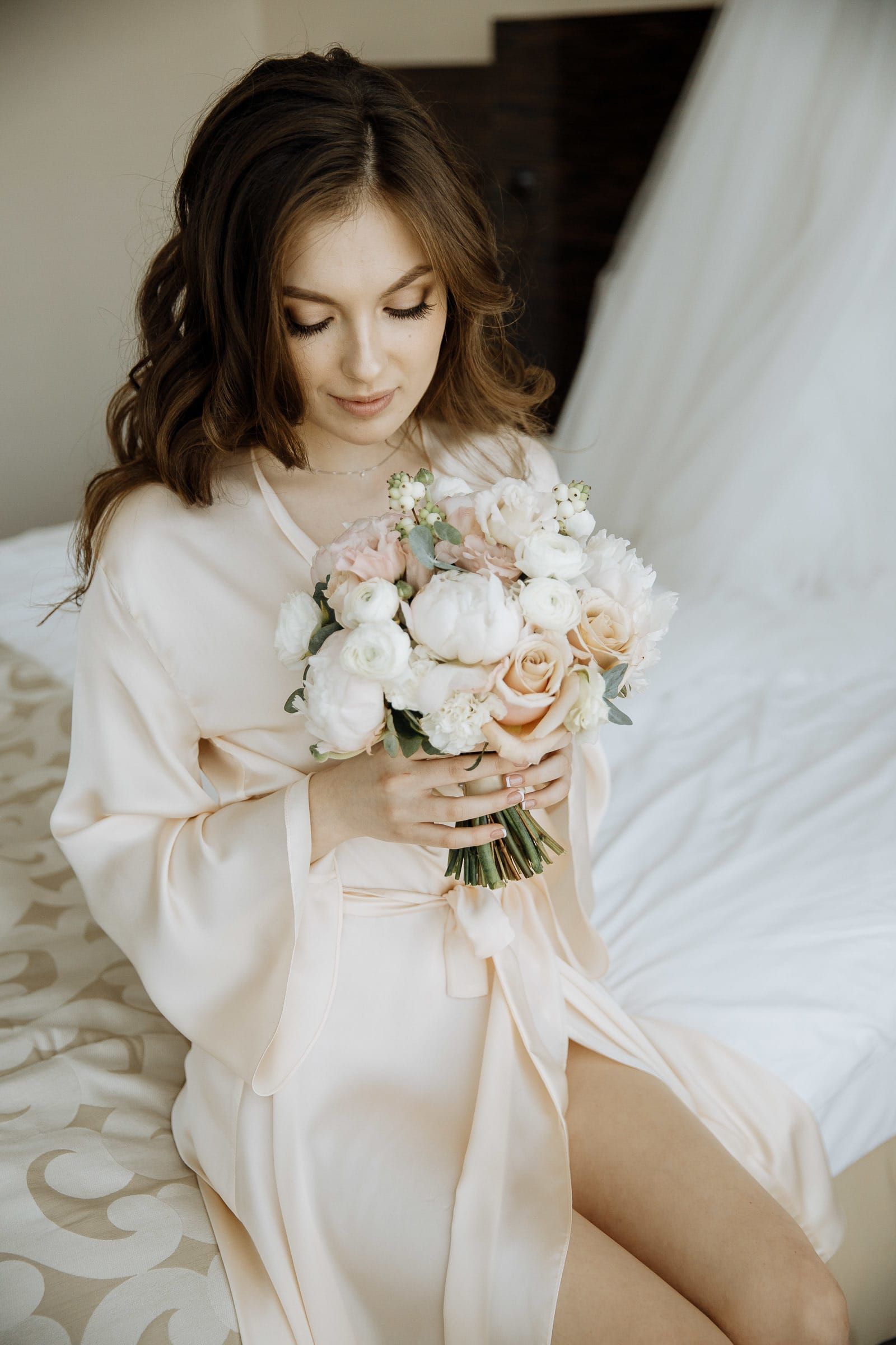 A candid, natural light portrait of a bride in a white silk robe during morning preparations in Bude.
