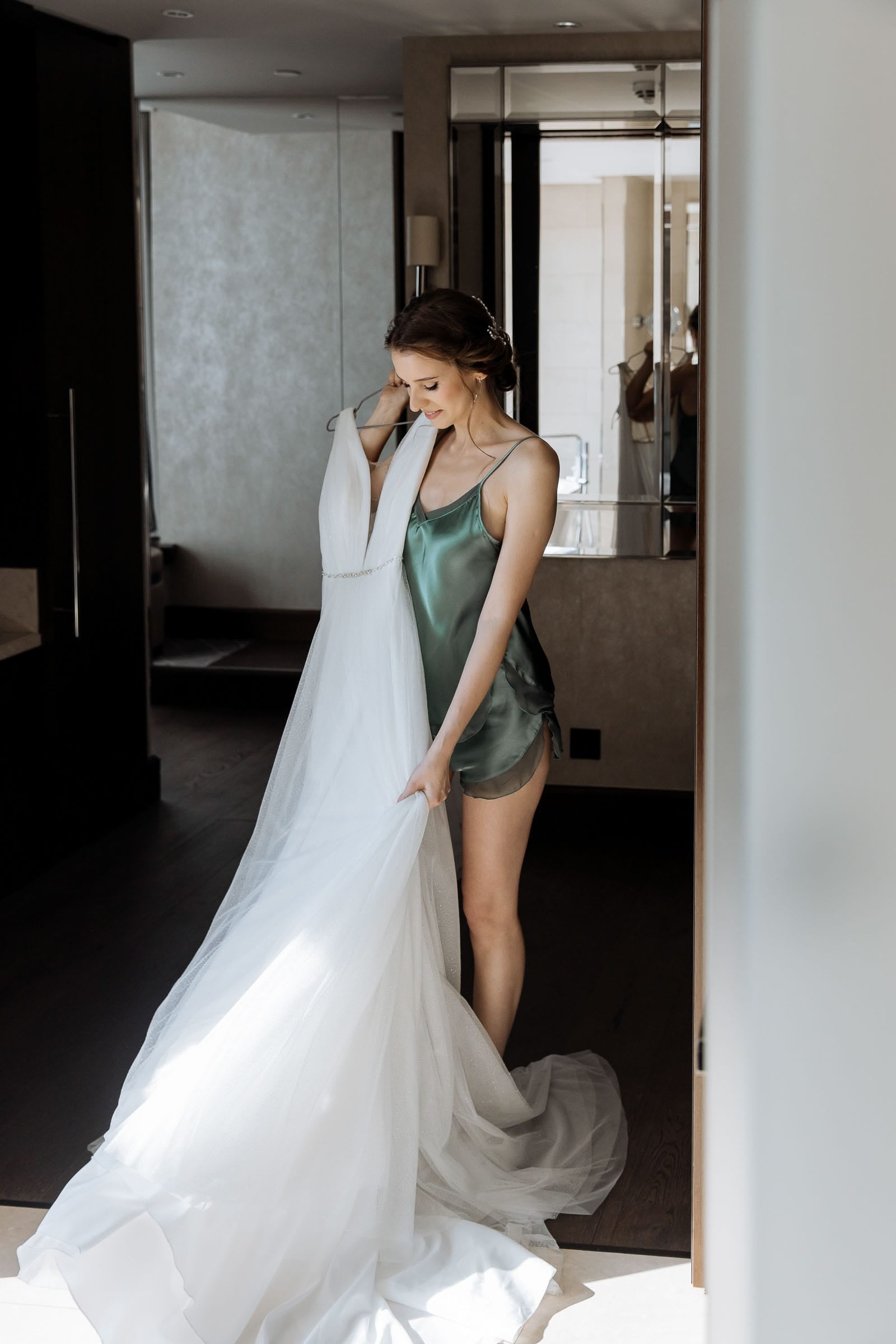 A bride holding her wedding dress against a window, captured by Cornwall photographer Tanya Bogdan.
