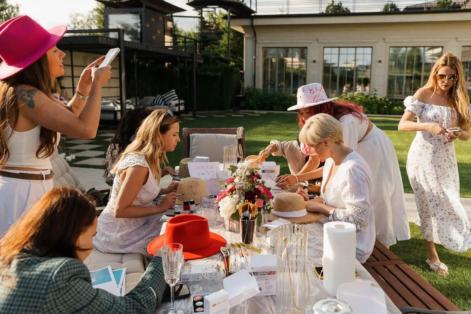 Guests enjoying a custom hat-painting activity at a luxury garden party, by Cornwall photographer Tanya Bogdan.