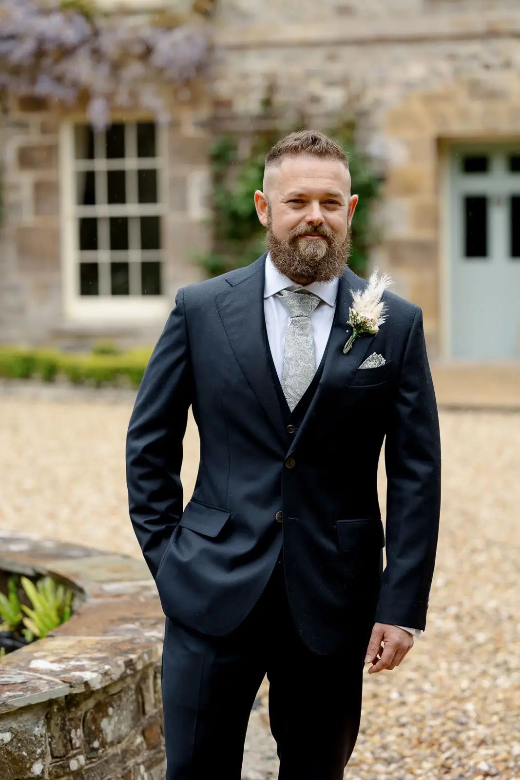 The groom poses for a relaxed wedding portrait outside Glebe Barn in Devon.