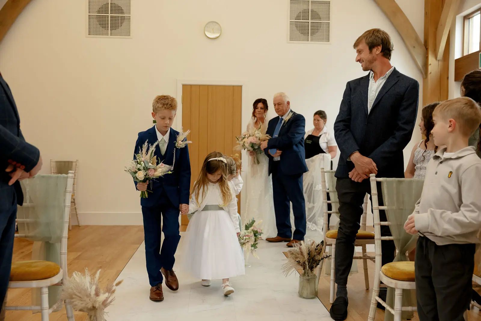 The page boy and flower girl walk down the aisle during the wedding ceremony at Glebe Barn.