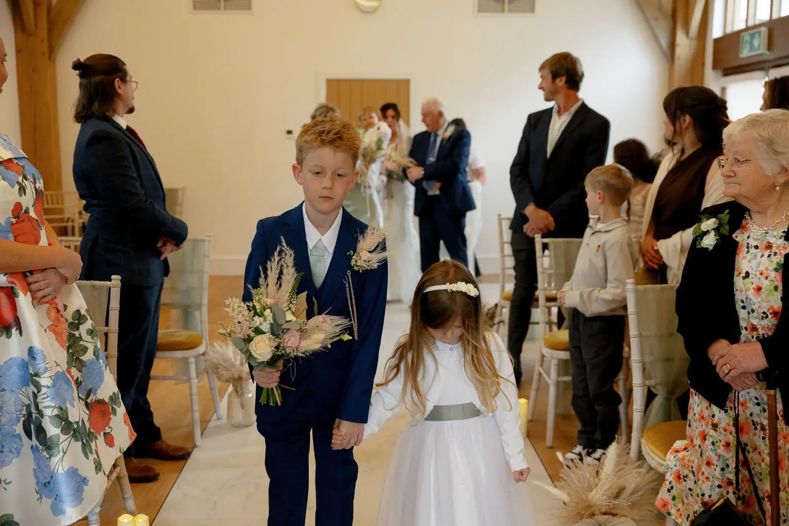 The page boy and flower girl stand together during the wedding ceremony at Glebe Barn.
