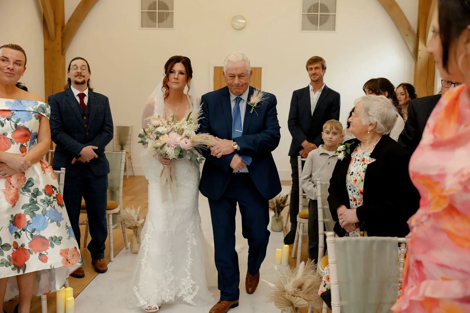 The bride walks down the aisle with her father during the wedding ceremony at Glebe Barn.