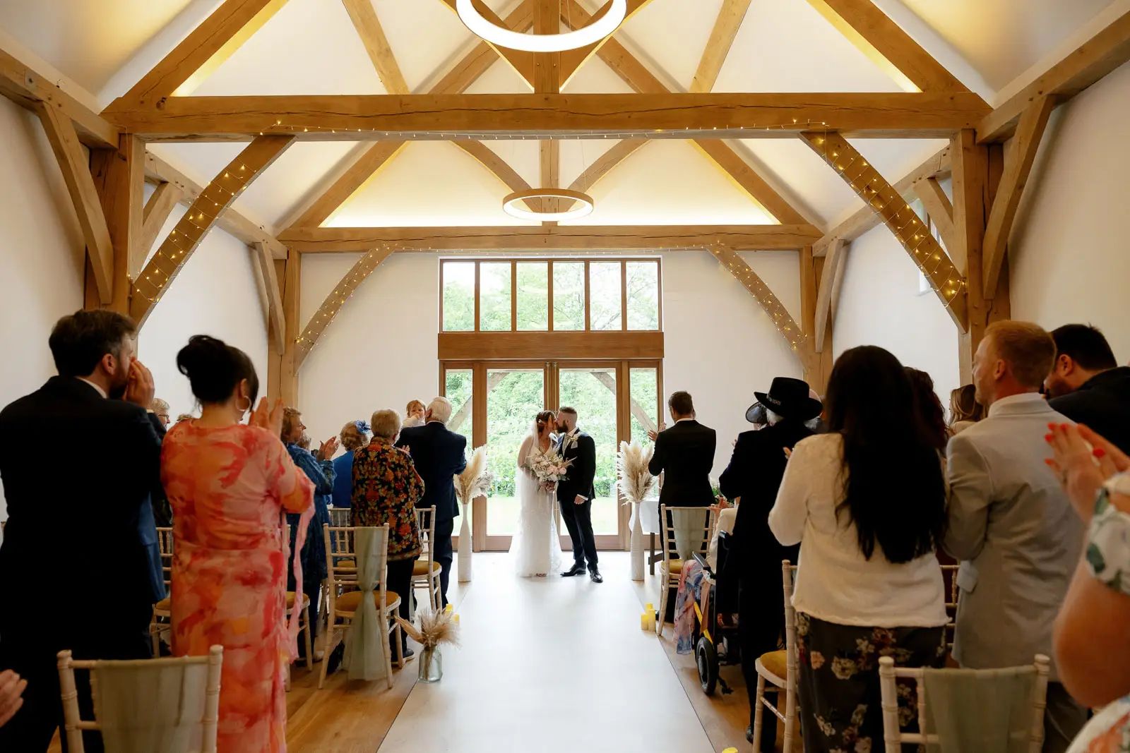 The bride and groom stand at the front of the timber-framed wedding ceremony at Glebe Barn in Devon by Tanya Bogdan Photography