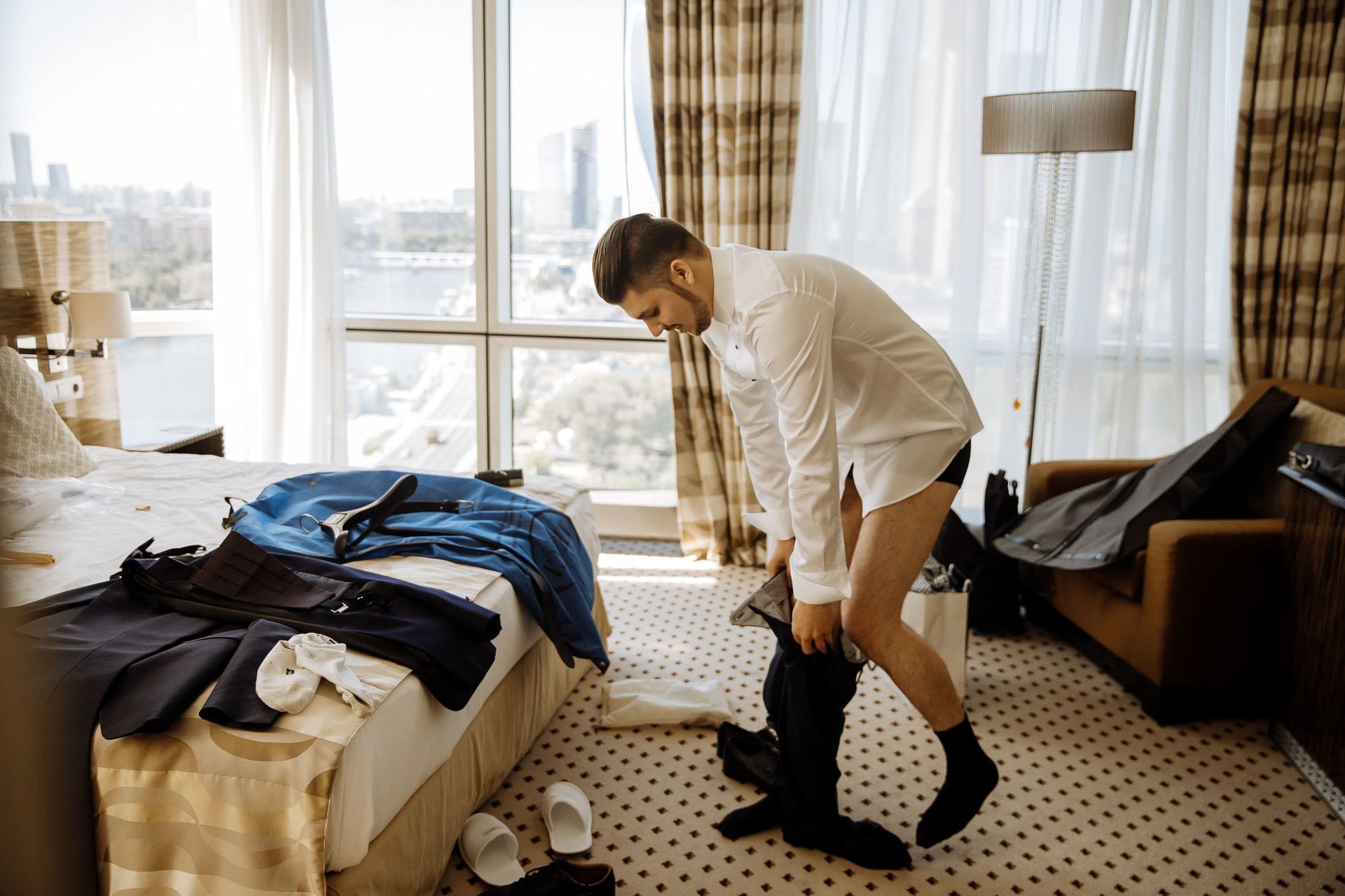 Documentary-style shot of a groom putting on his wedding trousers, by a wedding photographer, Tanya Bogdan.