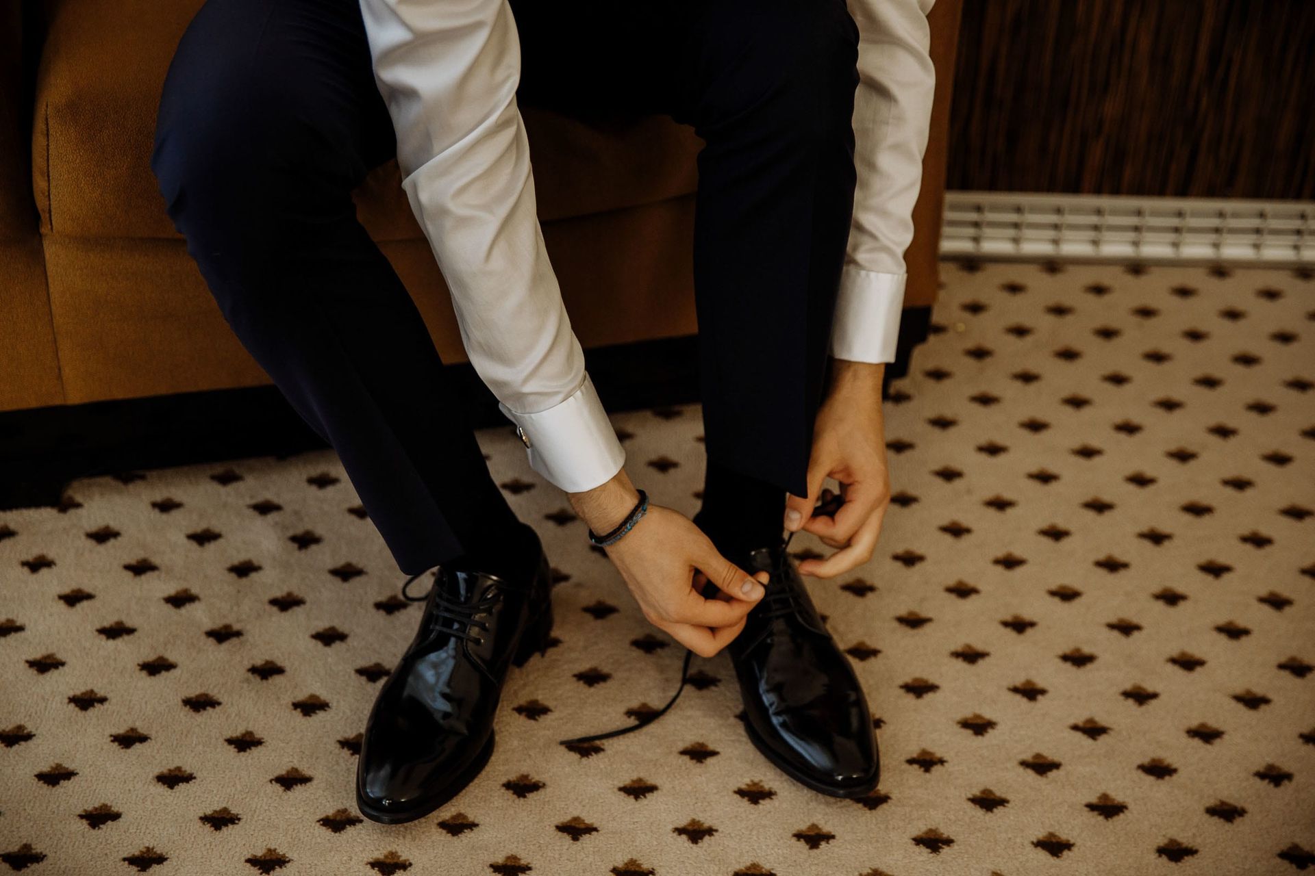 Close-up of a groom in a tuxedo adjusting his leather wedding shoes.