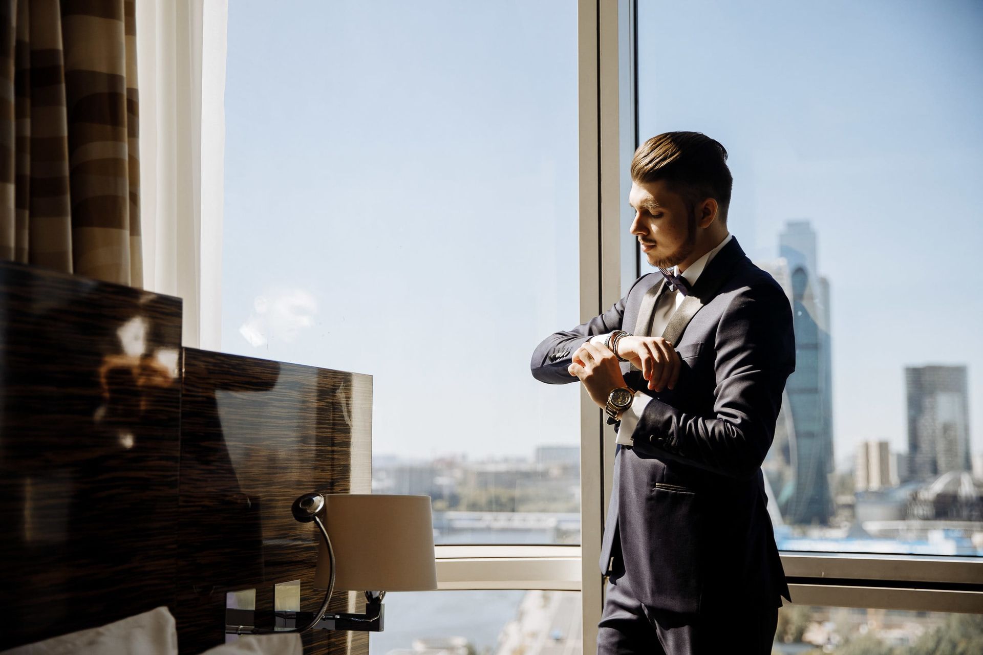 Groom adjusting his cufflinks against a blurred city backdrop, by a wedding photographer, Tanya Bogdan.