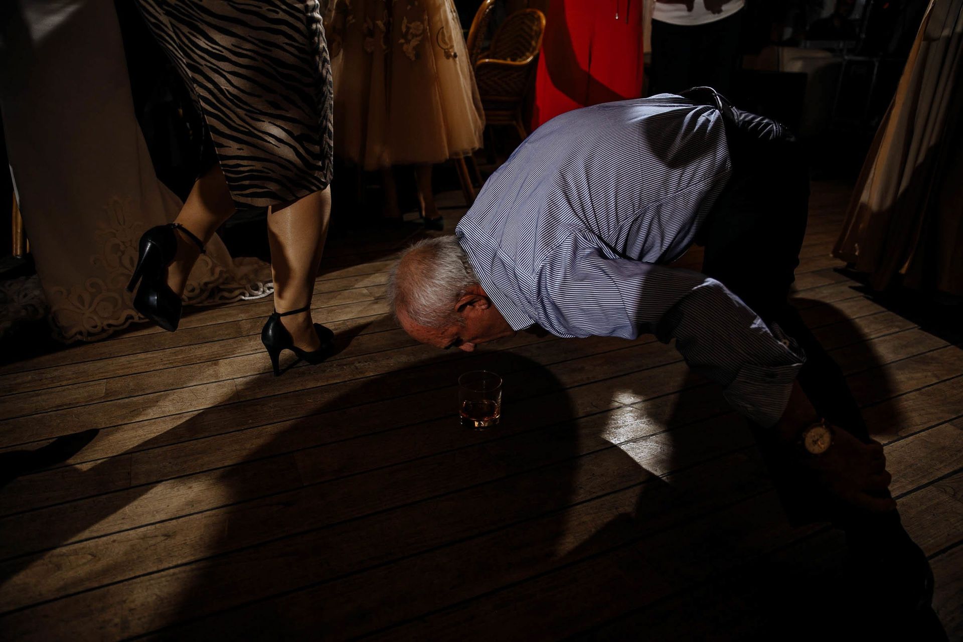 Fun candid dance floor father of the bride picking up drink with mouth by Bude wedding photographer Tanya Bogdan.