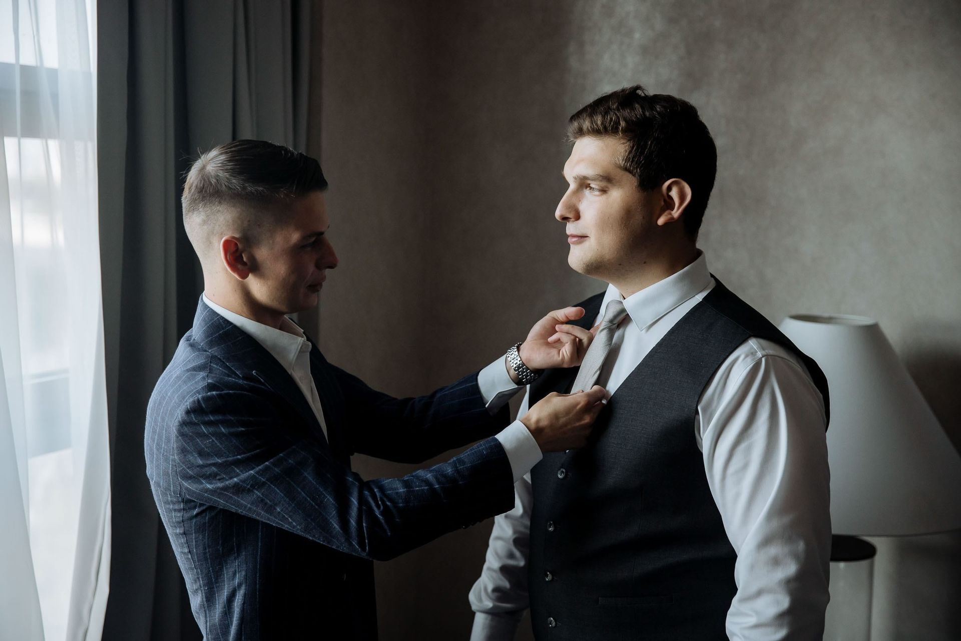 Candid moment of a groomsman helping the groom with his suit, photographed by Cornwall wedding photographer Tanya Bogdan.