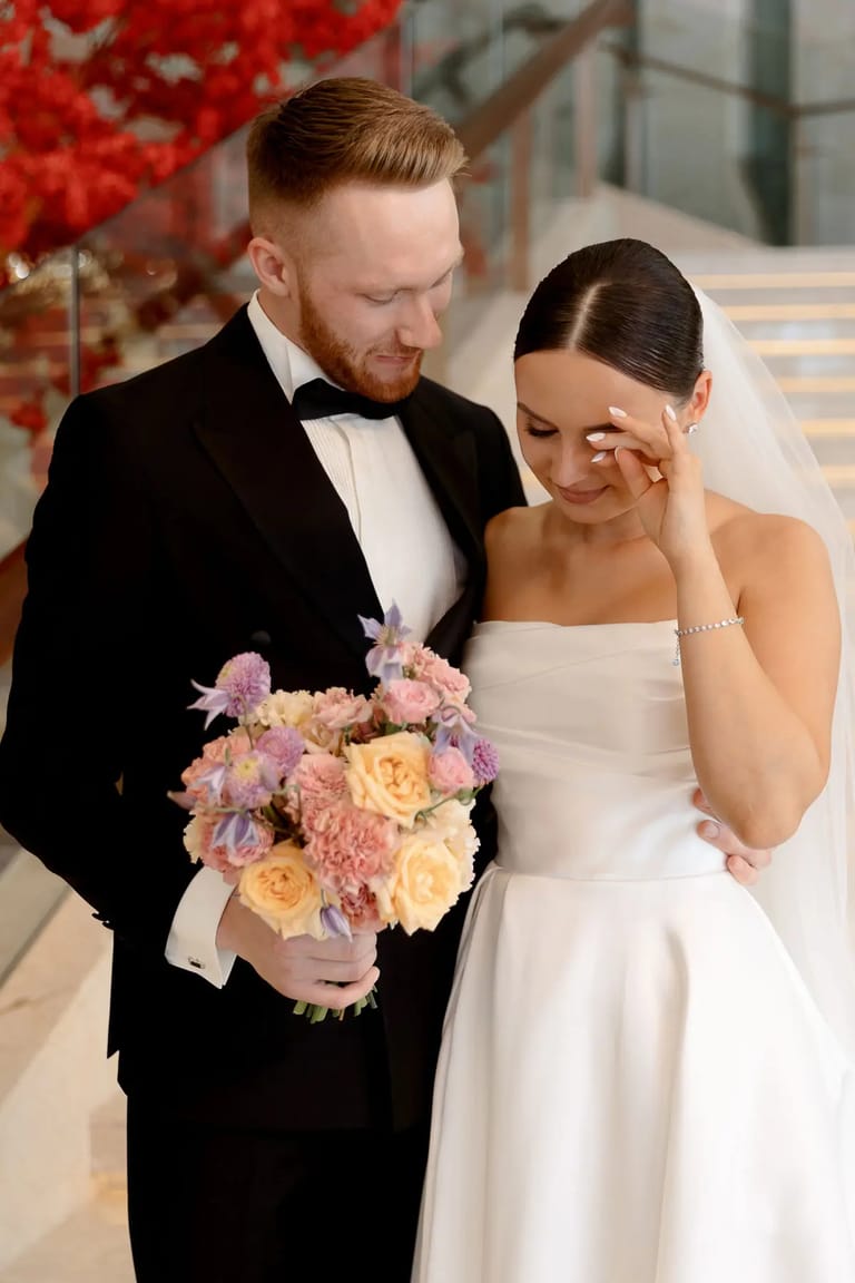 A touching, documentary-style photo of a bride wiping away a tear while holding a pastel bouquet, taken by Tanya Bogdan, a wedding photographer serving Devon and London.