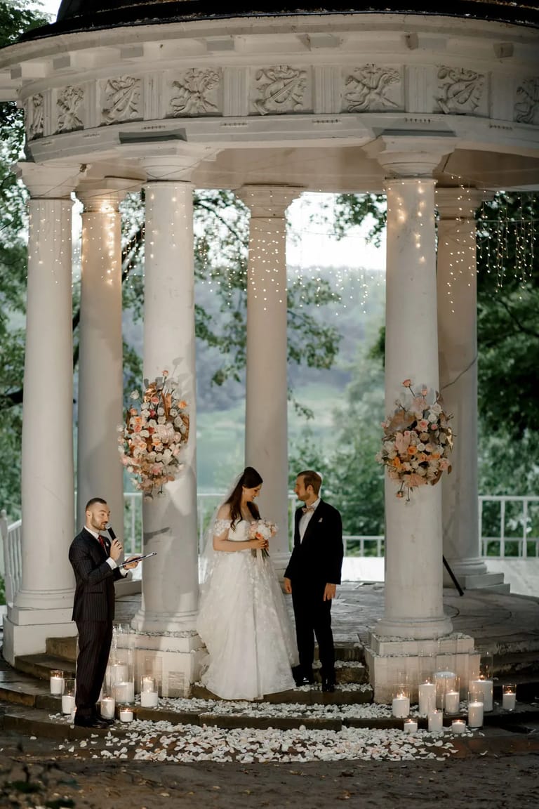 Romantic outdoor wedding ceremony held under a white classical pavilion with floral arrangements and candles by London wedding photographer Tanya Bogdan