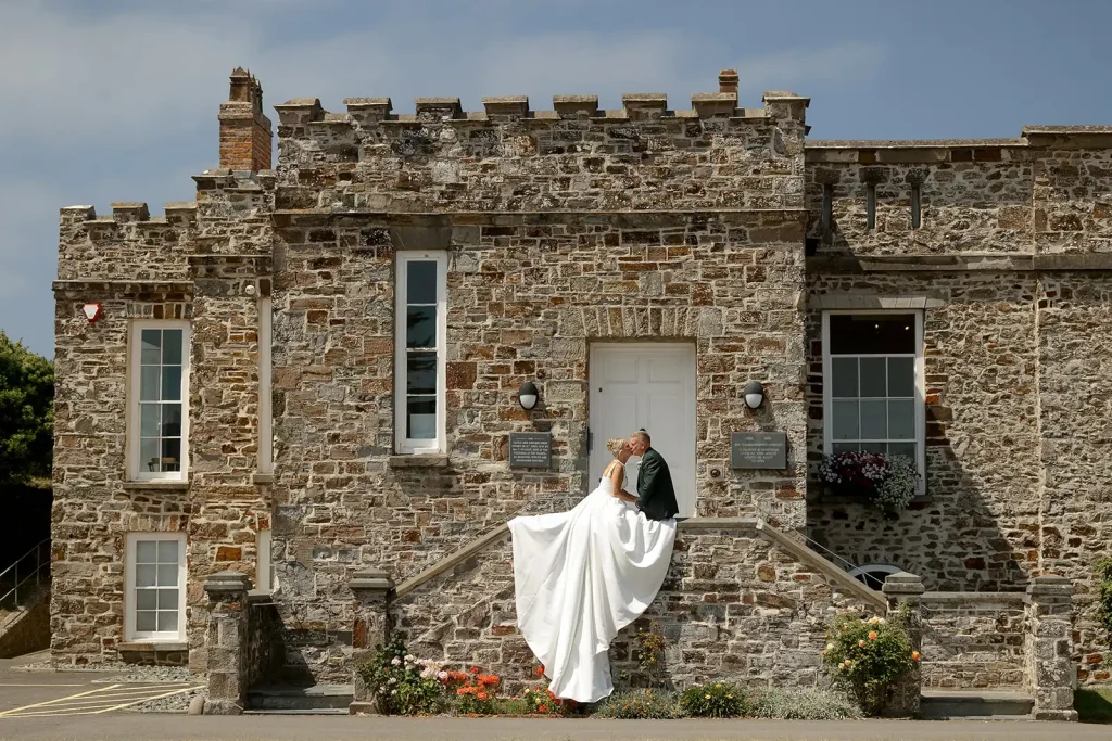 Bride sitting on a stone wall displaying her wedding dress train at Bude Castle, photographed by Tanya Bogdan