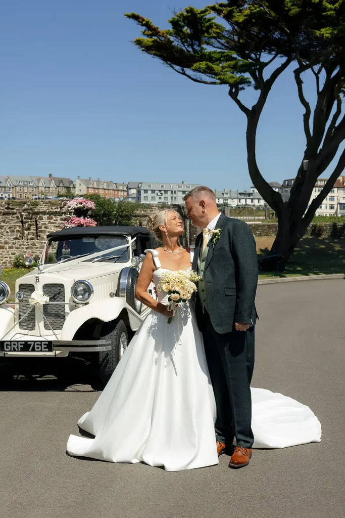Bride and Groom standing in front of a classic car looking into each other's eyes at Bude Castle