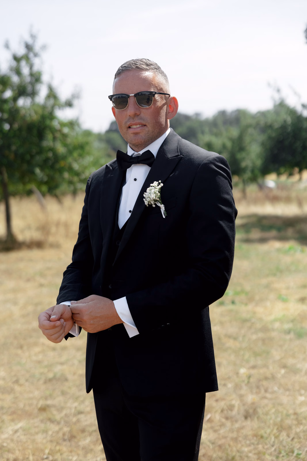 Groom portrait suit adjusting cuff at a family farm wedding in Taunton