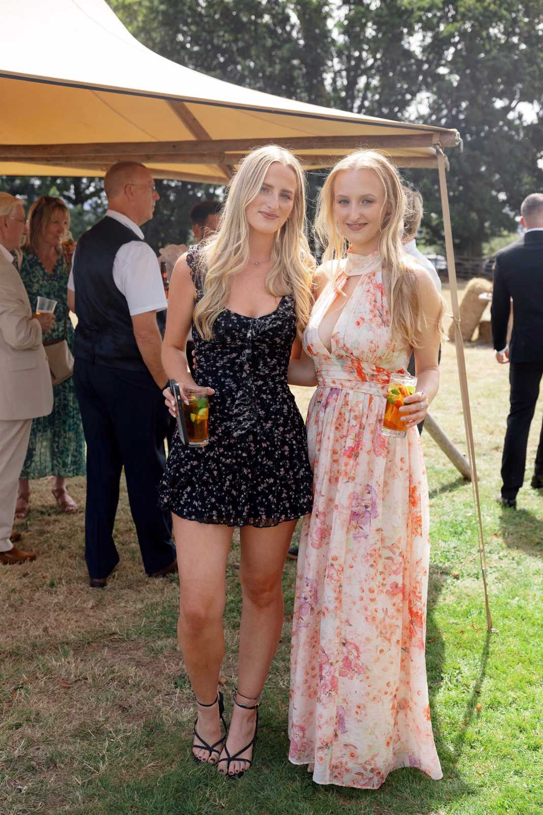 Two guests summer dresses with drinks at a family farm wedding in Taunton