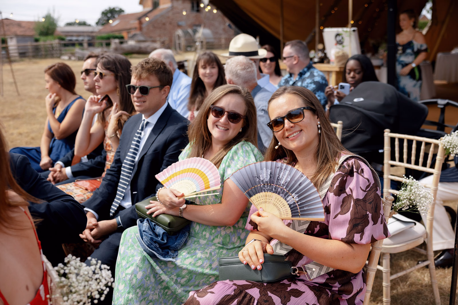 Guests with hand fans waiting for ceremony at a family farm wedding in Taunton