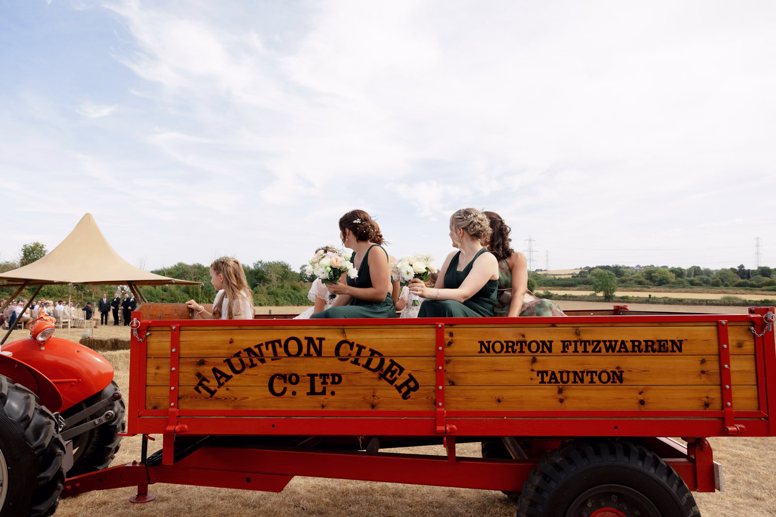 Bridesmaids riding red vintage tractor trailer at a Taunton farm wedding, photographed by Tanya Bogdan Photography
