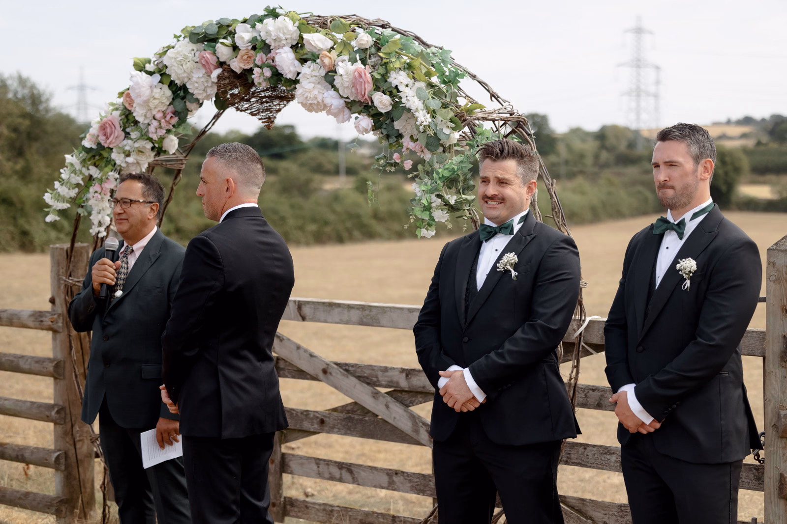 Groom and groomsmen waiting at floral arch ceremony at a family farm wedding in Taunton