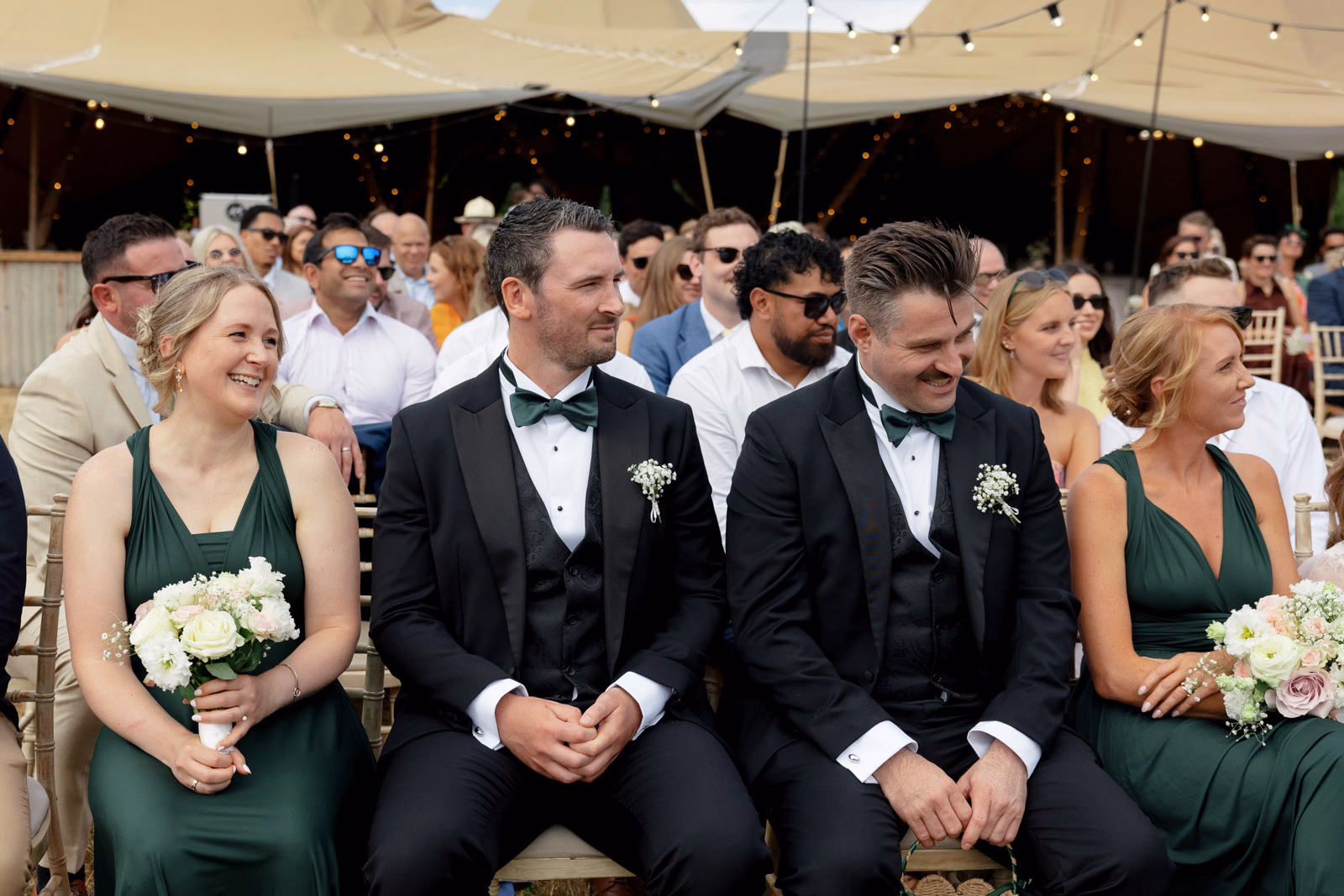 Bridesmaids and groomsmen smiling during ceremony at a Taunton farm wedding, photographed by Tanya Bogdan Photography