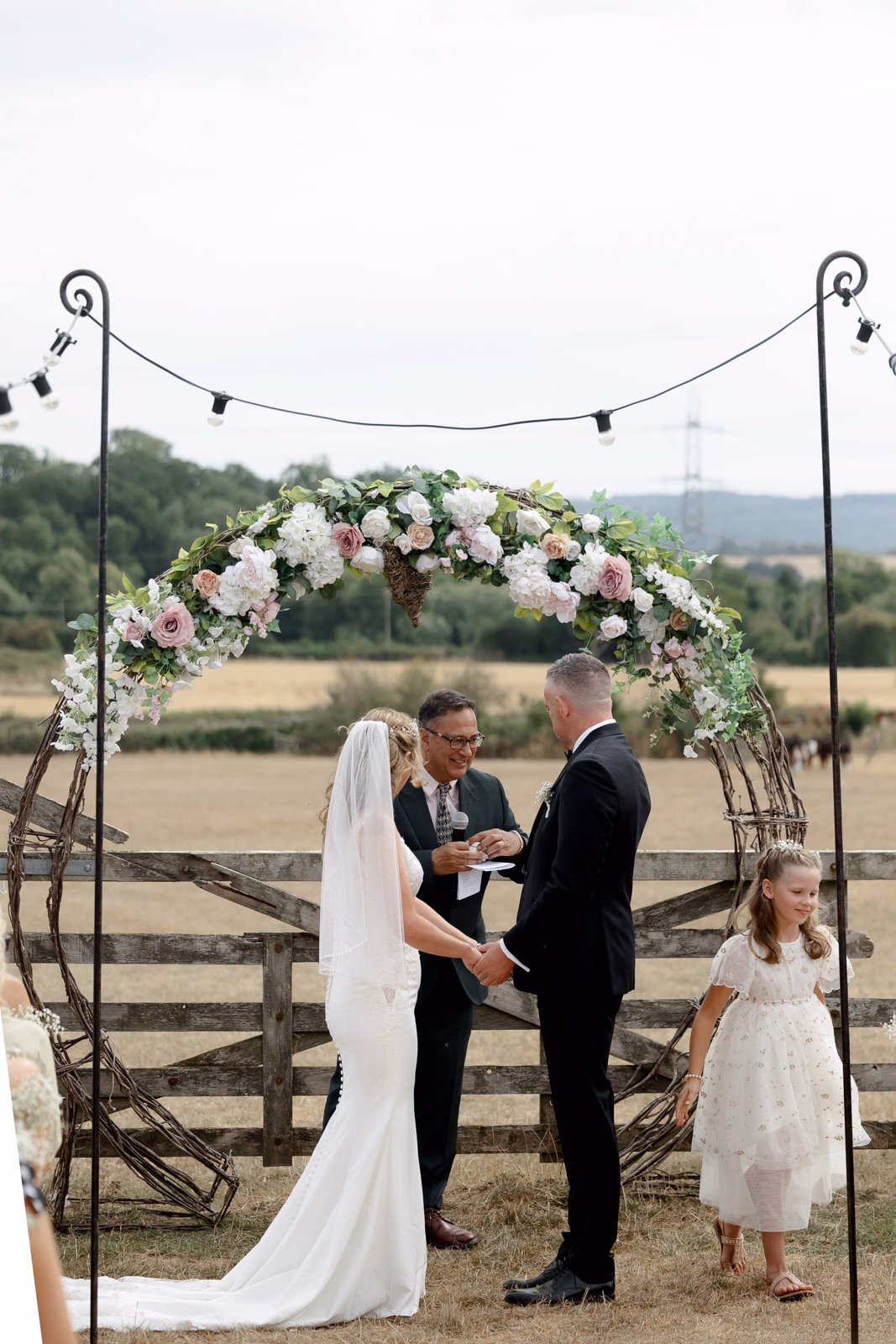 Bride groom and flower girl ceremony arch at a family farm wedding in Taunton