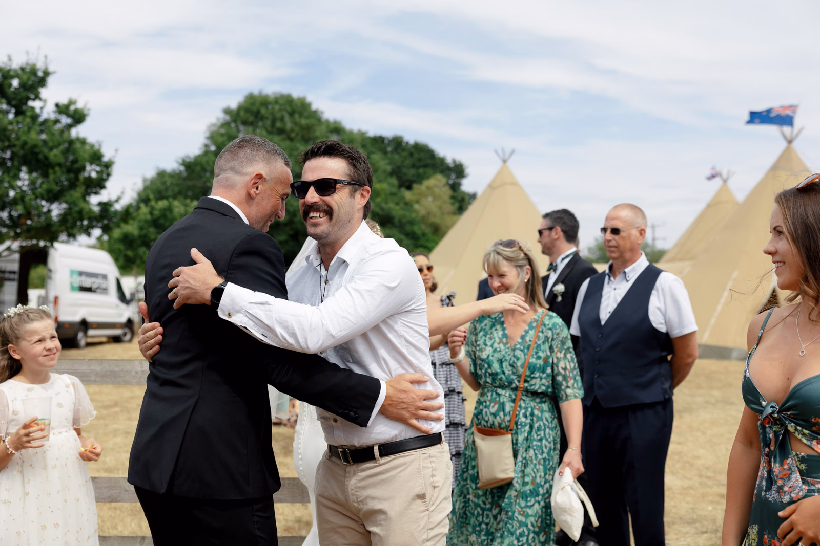 Groom hugging friend tipis background at a family farm wedding in Taunton