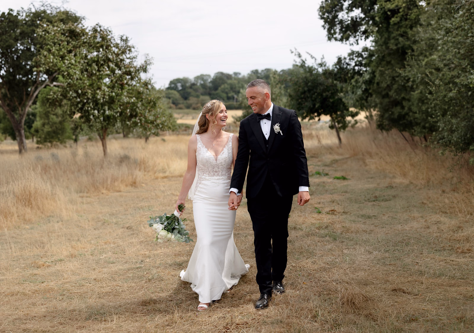 Bride and groom walking wide view orchard at a family farm wedding in Taunton