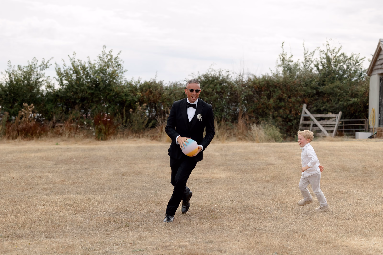Groom and child playing in field at a family farm wedding in Taunton