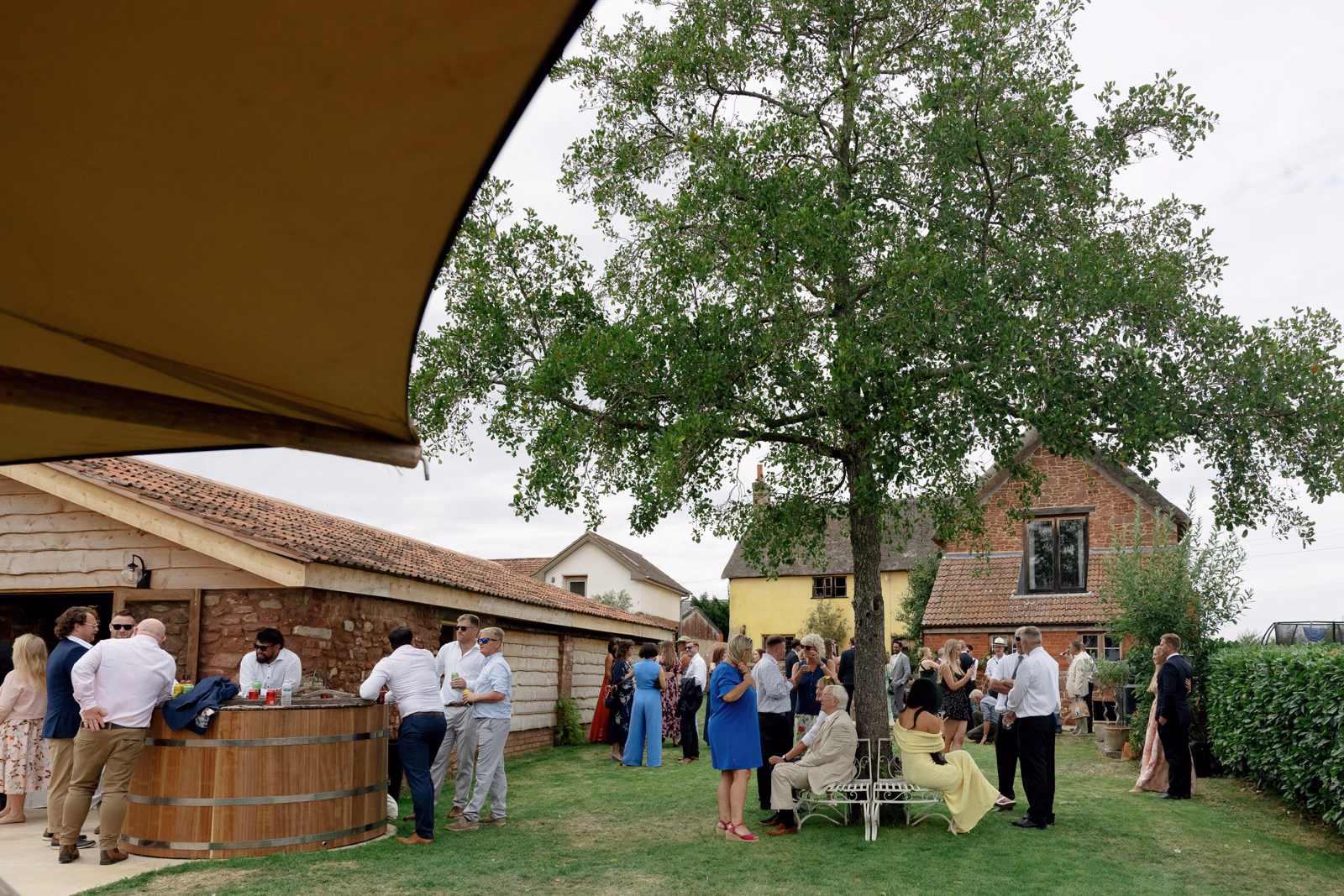 Guests by farm buildings garden at a family farm wedding in Taunton