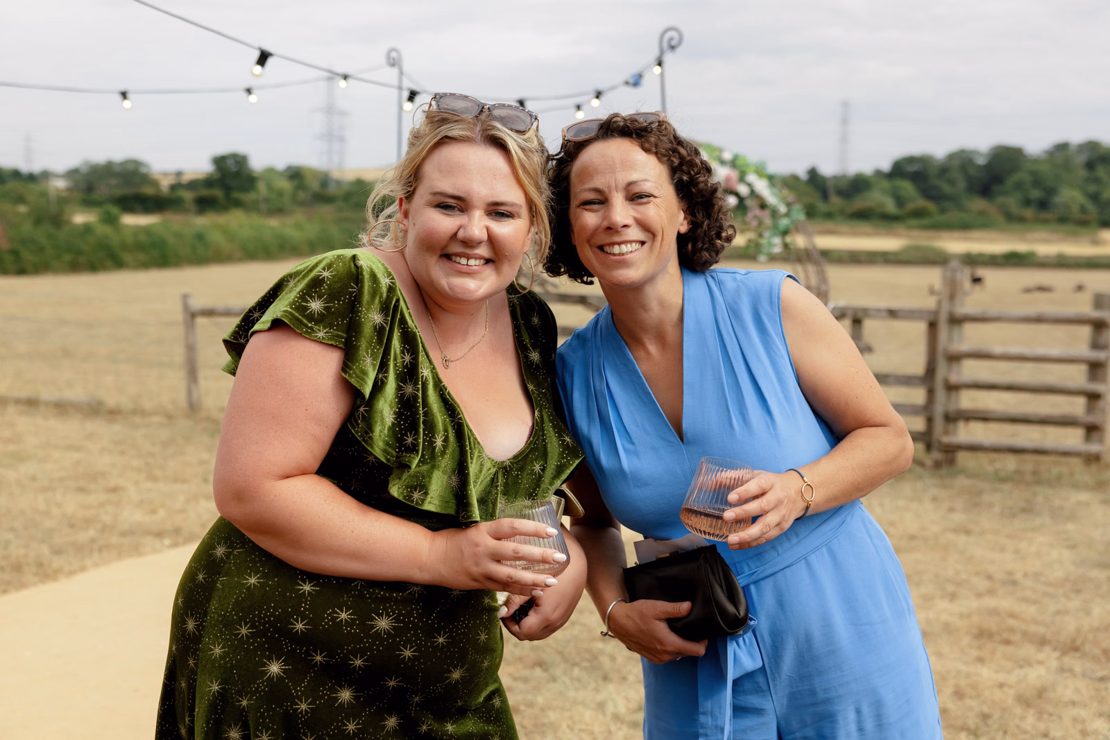 Two friends smiling with drinks at a Taunton farm wedding, photographed by Tanya Bogdan Photography