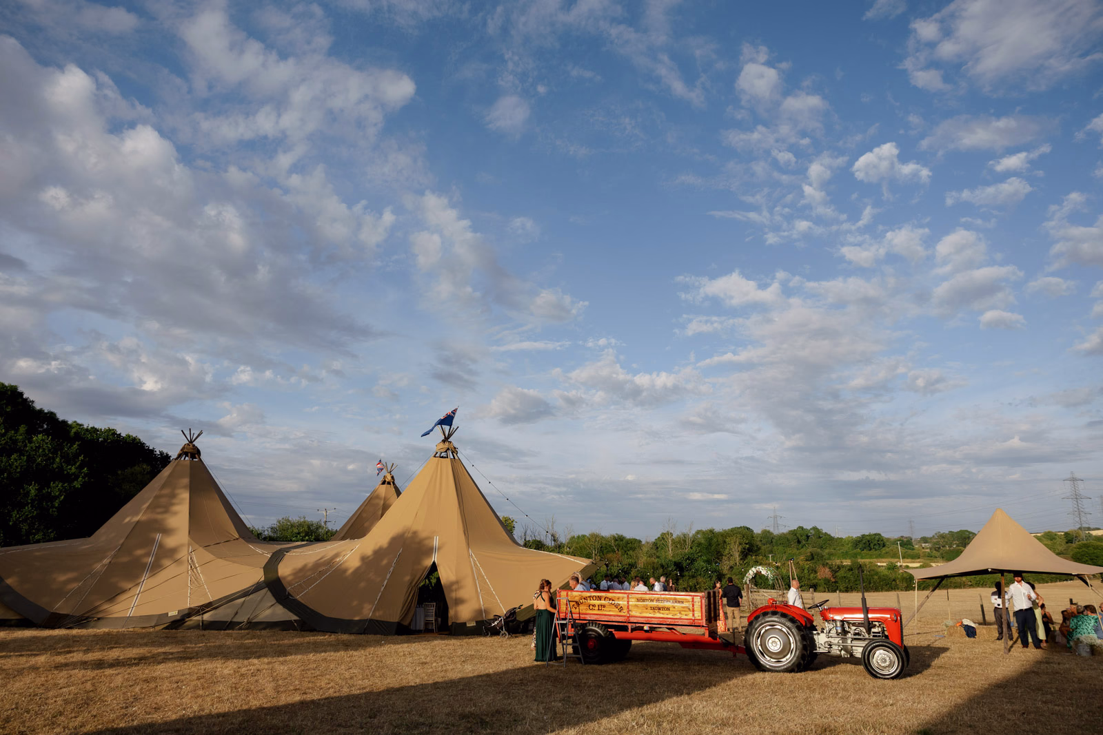Tractor trailer and tipis sunset sky at a family farm wedding in Taunton