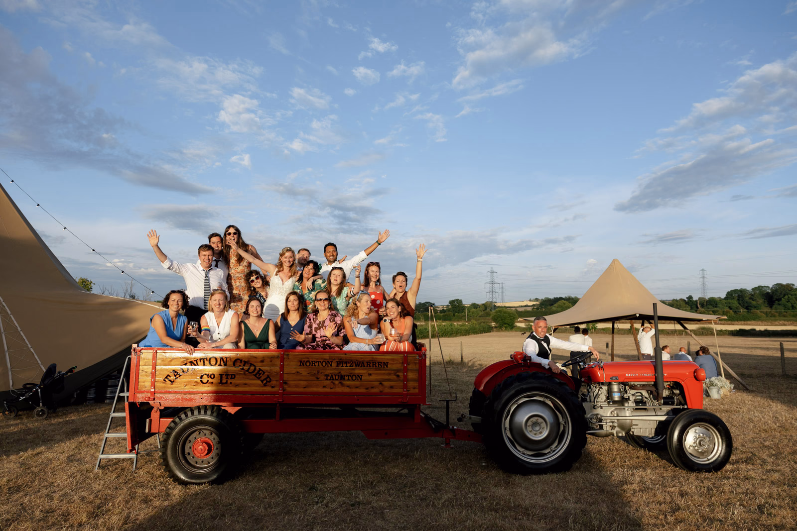 Guests on tractor trailer waving at a Taunton farm wedding, photographed by Tanya Bogdan Photography